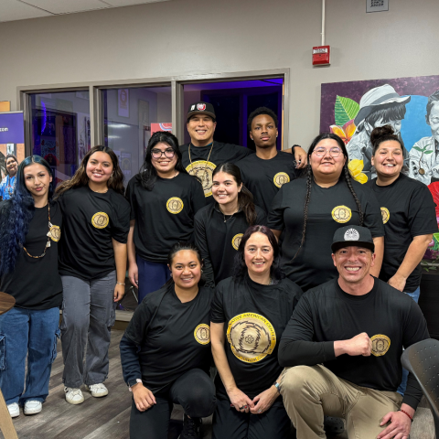 11 people smiling at the camera standing together. All are wearing black shirts with the NAC logo.